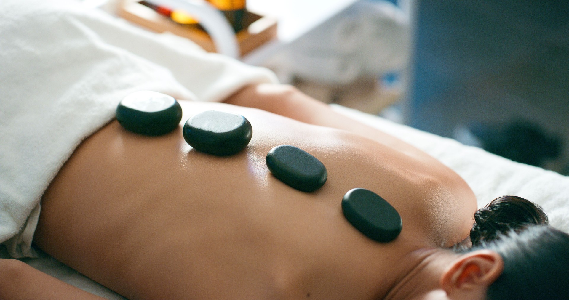 Woman, relax and hot stone massage in spa for wellness, muscle tension and stress relief with heat application. Female person, rocks and therapeutic healing in resort for back pain, zen and self care