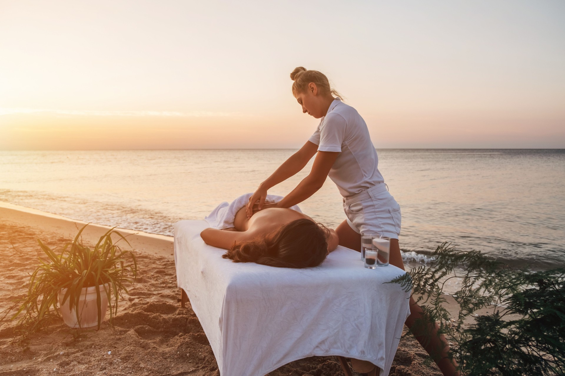 Young masseuse doing massage by the sea at sunrise